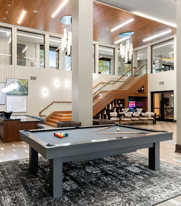 A pool table is in the middle of a room with a staircase in the background.