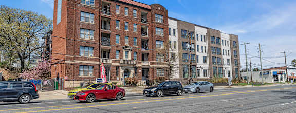 A red car is parked on the side of the road in front of a brick building.