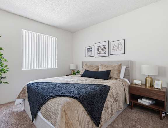 A bedroom with a bed, nightstand, and a plant.