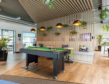 A pool table is in the middle of a room with a wooden floor and a ceiling with wooden slats.