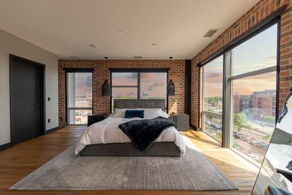 a bedroom with a bed and exposed brick walls and large windows