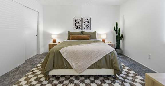 A bedroom with a bed, two lamps, and a cactus.