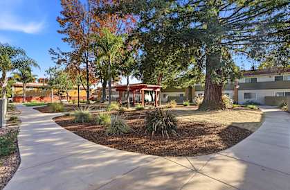 A tree-lined walkway leads to a building with a red roof.