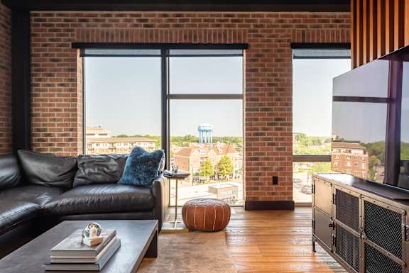 a living room with a black leather couch and a tv and a brick wall