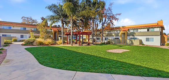 A building with a red roof is surrounded by a green lawn and palm trees.