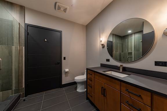 A bathroom with a black door, a white toilet, and a round mirror.