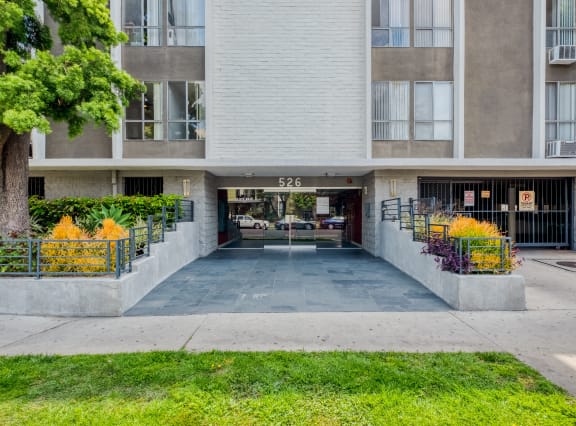 the entrance to an apartment building with a yard and a tree in front of it