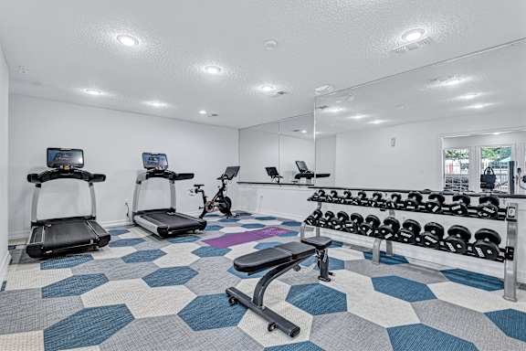 A gym with a variety of equipment including treadmills, a stationary bike, and a bench press.