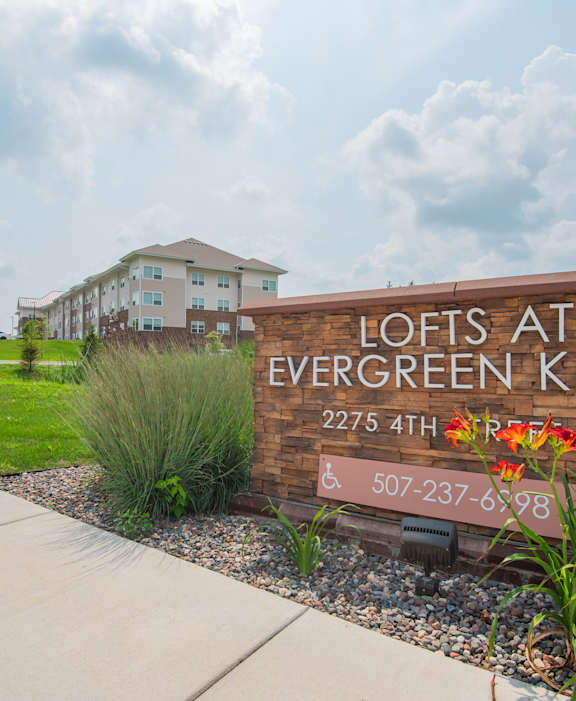 A brick sign that says Lofts at Evergreen Knoll in front of a building.