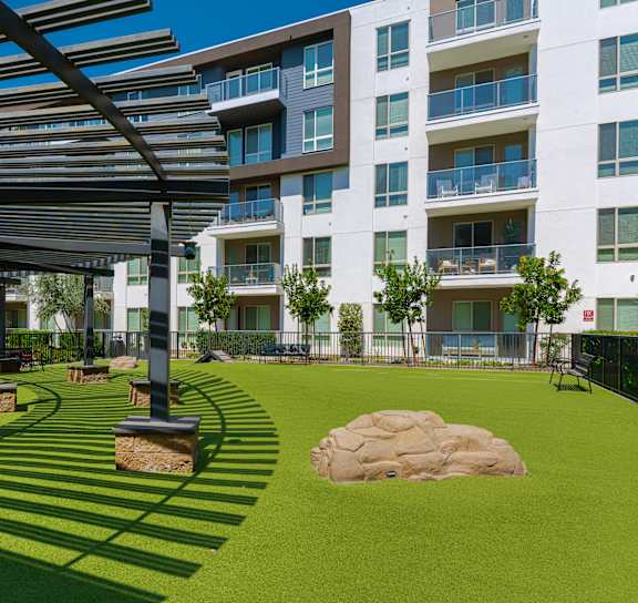 A large grassy area with a shaded walkway in front of apartment buildings.