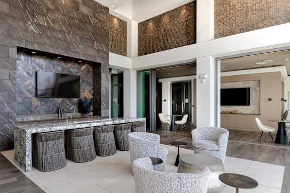 A modern living room with a stone fireplace and grey chairs.