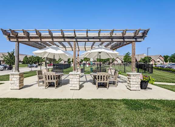 A wooden pergola with two umbrellas provides shade for a picnic table and chairs.