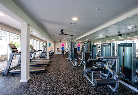 A spacious gym with treadmills, exercise machines, and a ceiling fan.