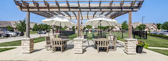 A wooden pergola with two umbrellas provides shade for a picnic table and chairs.