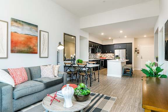 A modern living room with a grey couch and a dining area in the background.