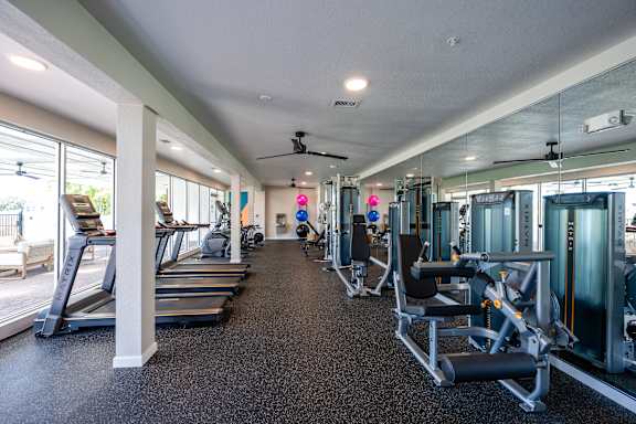 A spacious gym with treadmills, exercise machines, and a ceiling fan.