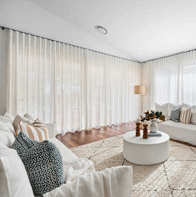 a living room with white curtains and a white couch and a coffee table
