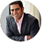 A man in a black jacket and pink shirt is smiling.