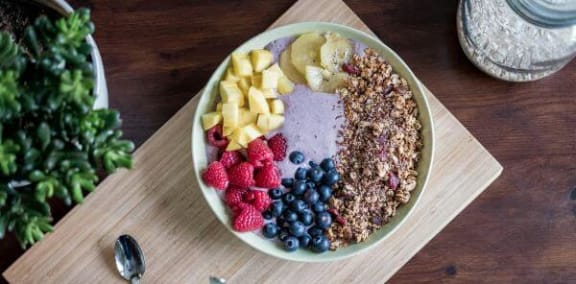 a bowl of cereal and fruit on a wooden table