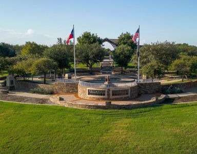 A circular stone structure with two flags on top is surrounded by a grassy area at Civic at Frisco Square Apartments, Frisco, TX, 75034