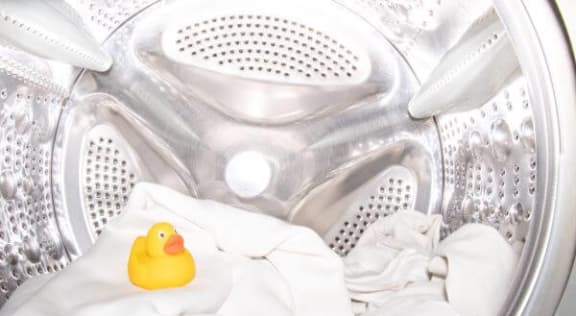 a yellow rubber duck sitting on top of a white shirt in a washing machine
