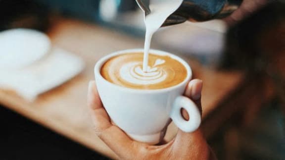 a person pouring milk into a cup of coffee