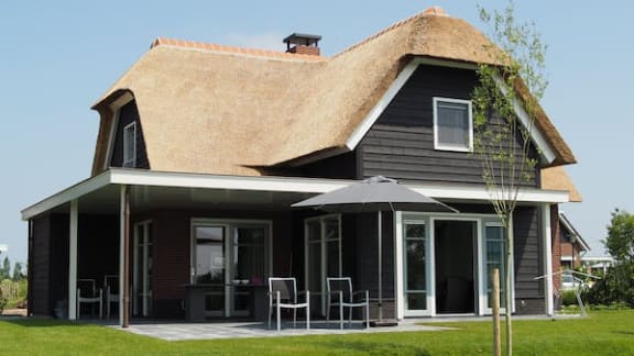 a house with a thatched roof and a patio with chairs and an umbrella