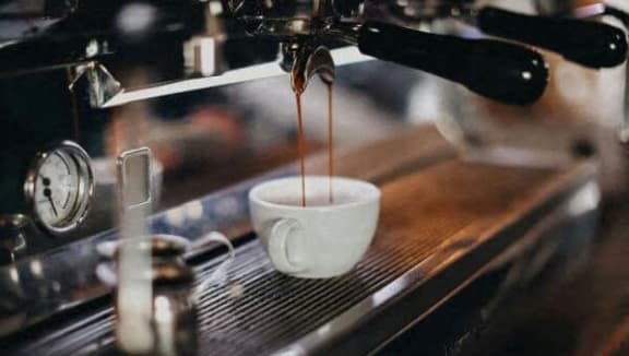 a cup of coffee being poured from a espresso machine