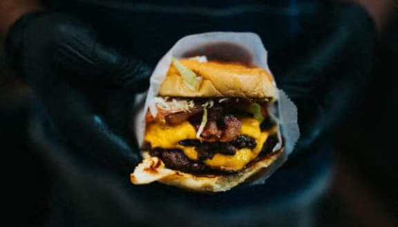 a hand holding a sandwich with meat and cheese