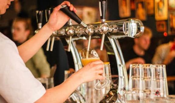 a person pouring a glass of beer in a bar