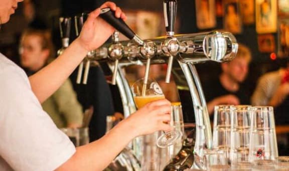 a person pouring a glass of beer in a bar