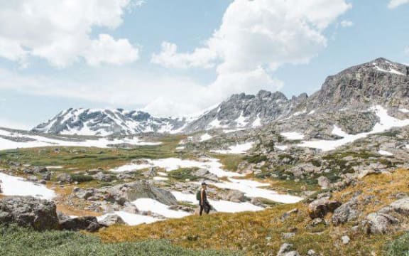 a man standing on a hill with snow covered mountains