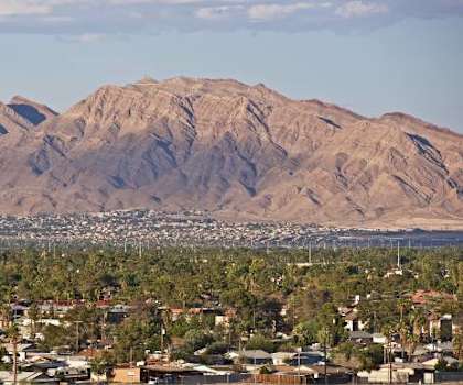 A mountain looms over a cityscape with buildings and palm trees.
