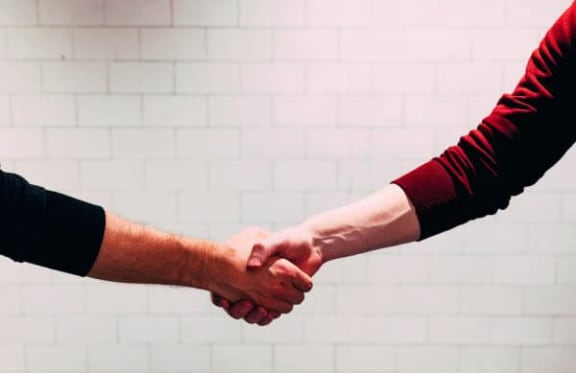 two people shaking hands in front of a white wall