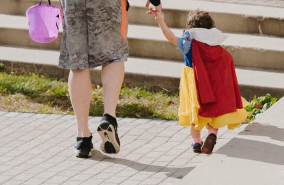 a woman and a child in costumes walking on a sidewalk