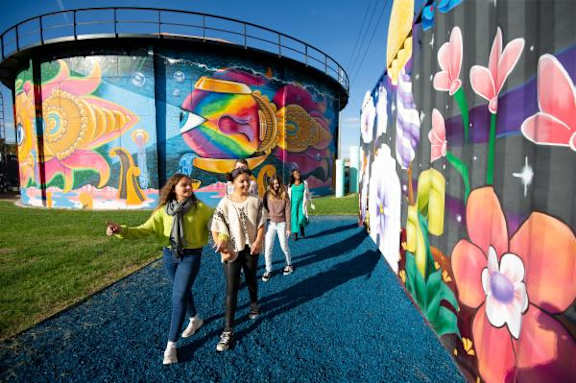 Three people are walking in front of a colorful mural at AVIA North Shore Apartments, Jeffersonville