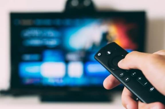 a hand holding a remote control in front of a tv
