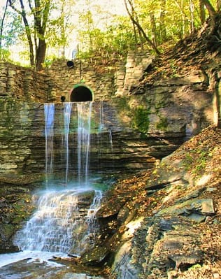 a waterfall in the woods near a tunnel