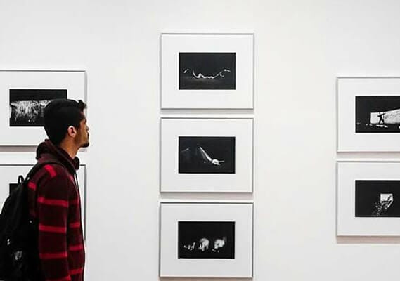 a man in a red and black shirt is looking at pictures on a wall