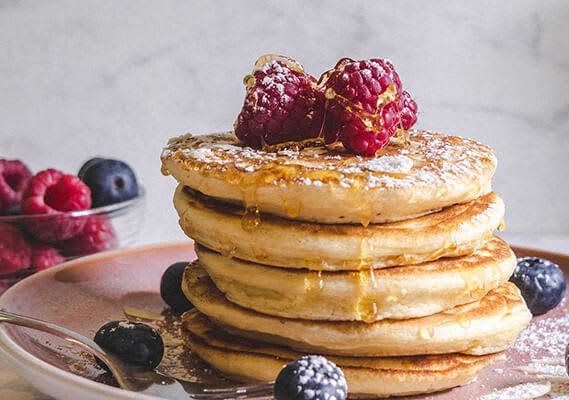 A stack of pancakes topped with raspberries and blueberries.