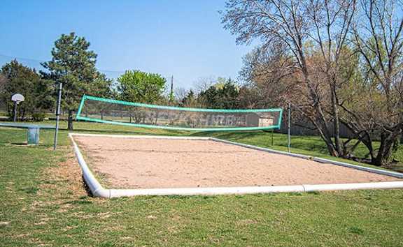 A sand volleyball court with a green net and white boundary lines.