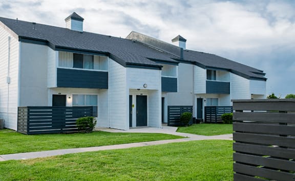 a white apartment building with blue shutters and a green lawn
