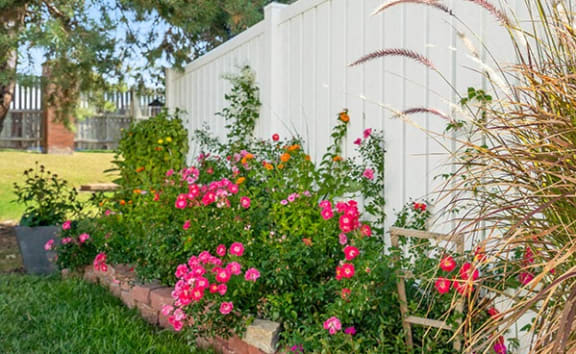a flower garden in front of a white fence