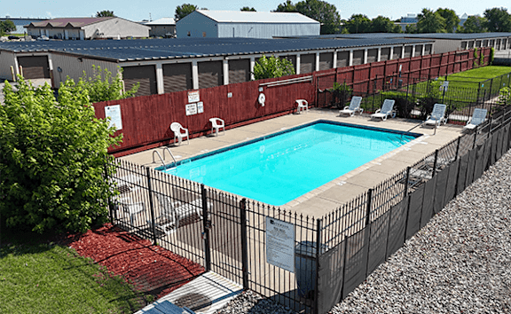 A pool surrounded by a black fence and red gravel.