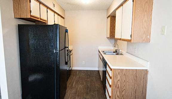 A black fridge and wooden cabinets in a small kitchen.