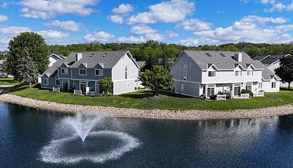 A fountain in the middle of a lake in front of a house.