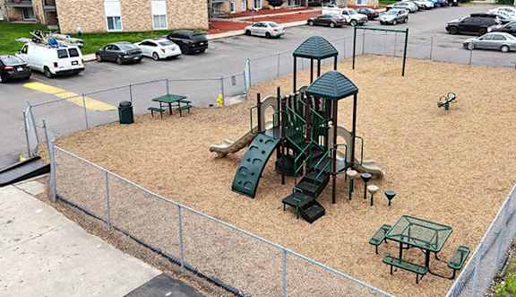 A playground with a green slide and a fence.