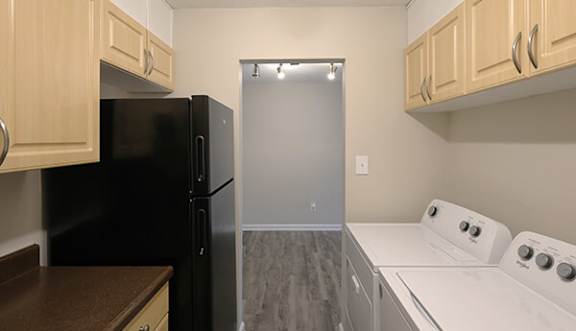 A black refrigerator sits in a kitchen with wooden cabinets and a white dishwasher.
