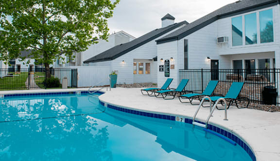 a swimming pool with blue chaise lounge chairs and a building in the background