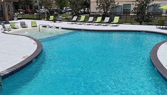 A swimming pool with a black fence and green chairs.